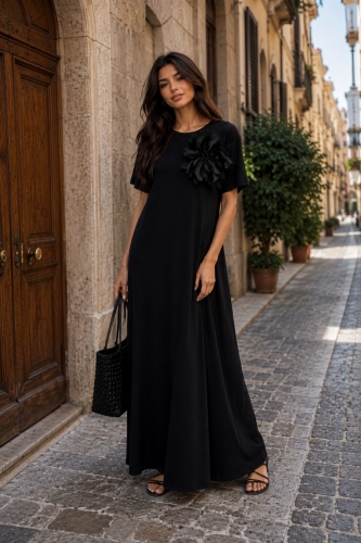 Czarna sukienka maxi z odpinanym kwiatem przyciąga uwagę minimalistyczną formą i eleganckim charakterem.